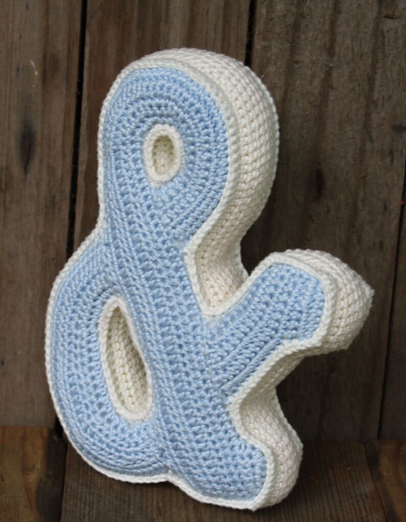 May include: A crocheted ampersand pillow in light blue and white. The pillow is shaped like the ampersand symbol and has a textured surface.
