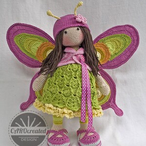 May include: Crocheted butterfly doll with pink wings, a green dress, and pink shoes. The doll has brown hair and is wearing a pink hat with a flower.
