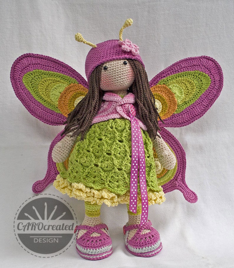 May include: Crocheted butterfly doll with pink wings, a green dress, and pink shoes. The doll has brown hair and is wearing a pink hat with a flower.