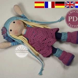 Puede incluir: Muñeca de crochet con cabello largo rubio, vistiendo un vestido rosa, un sombrero azul y botas azules y moradas. La muñeca está acostada sobre una superficie beige claro. La imagen incluye el texto "Crochet PDF Pattern".