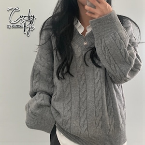 May include: A grey cable-knit jumper with a V-neck. The jumper has a relaxed fit and long sleeves. The brand name "Comfy Pjs by DANICA" is in the upper left corner. The jumper is worn over a white collared shirt.