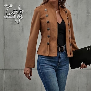 May include: A brown suede jacket with multiple dark buttons and a mandarin collar. The jacket is paired with blue jeans and a black top. The brand name "Comfy Pix by Danica" is visible in the upper left corner.