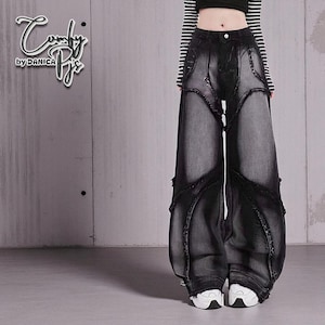 May include: Black denim wide-leg trousers with distressed detailing. The trousers feature a unique design with cut-out sections and decorative stitching. The text "Comfy by Danica" is in the upper left corner. The model is wearing a black and white striped top.