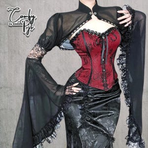 May include: A black sheer bolero with long sleeves and a high collar, paired with a red and black corset and a black skirt. The corset features intricate lace detailing. The outfit has a gothic aesthetic.