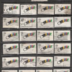 Puede incluir: Una colección de sellos postales antiguos con un diseño de bobsleigh y los anillos olímpicos en rojo, amarillo, verde y azul. Los sellos conmemoran los Juegos Olímpicos de Invierno de 1972 en Sapporo, Japón. Algunos sellos tienen marcas postales.