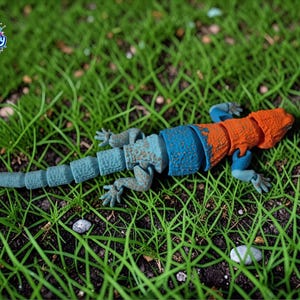 Peut inclure: Une figurine de lézard articulée avec une surface texturée, dotée d'une tête et d'un haut du corps orange vif, passant à une section médiane bleue et une queue bleue segmentée. Le jouet inclut le logo Toy Foundry dans le coin supérieur gauche.