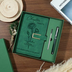 Puede incluir: Un juego de diario y bolígrafo verde en una caja de regalo. La portada del diario presenta las palabras "Chapter Thirty" y "Diana" con un diseño floral. Se incluye un bolígrafo plateado y una recarga de bolígrafo plateada.