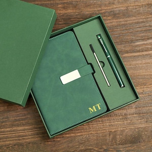 May include: A green leather-bound journal with a silver metal closure and the initials "MT" embossed in gold. The journal is packaged in a green box with a pen and a silver stylus.