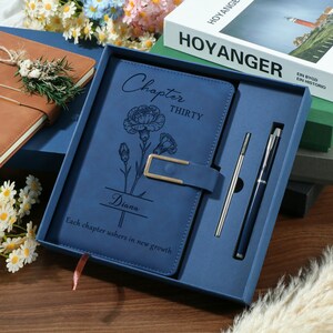 May include: A blue leather journal set in a gift box. The journal features a floral design and the name "Diana" engraved on the cover. Includes a pen and a ballpoint pen. The text on the journal reads "Chapter Thirty" and "Each chapter ushers in new growth."