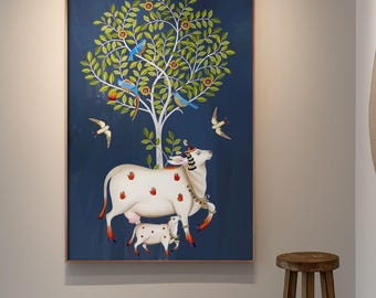 May include: An artistic painting on a dark blue background depicts a white cow with red spots, a calf, and a tree with birds. The painting is framed in a reddish-brown frame and hangs on a white wall in a gallery setting.