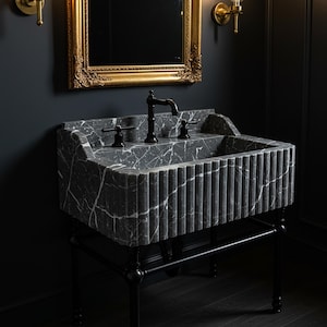 Pode incluir: Uma pia de banheiro de mármore preto com uma borda canelada e um suporte de metal preto. A pia tem duas torneiras pretas e um ralo preto.