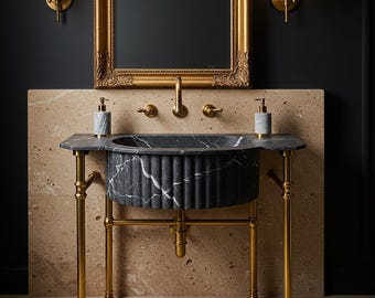 May include: A dark grey marble sink with a fluted exterior and white veining, supported by a brass metal frame. The sink features a brass tap, two matching soap dispensers, and is positioned beneath a gold-framed mirror with two wall sconces.