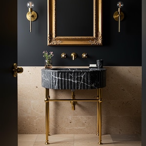 May include: A black marble bathroom sink with a gold stand. The sink has a fluted design and is set against a black wall with gold accents.