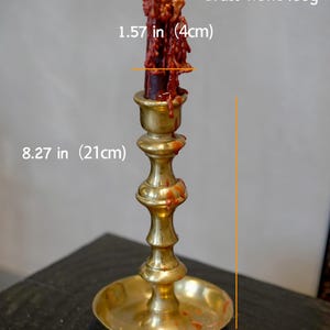May include: A brass candlestick holder with a lit dark red candle featuring dripping wax. The holder is 8.27 inches tall with a 4.33 inch base diameter. The candle diameter is 1.57 inches. The brass weight is listed as 1400g. Text reads Natasha Candle.
