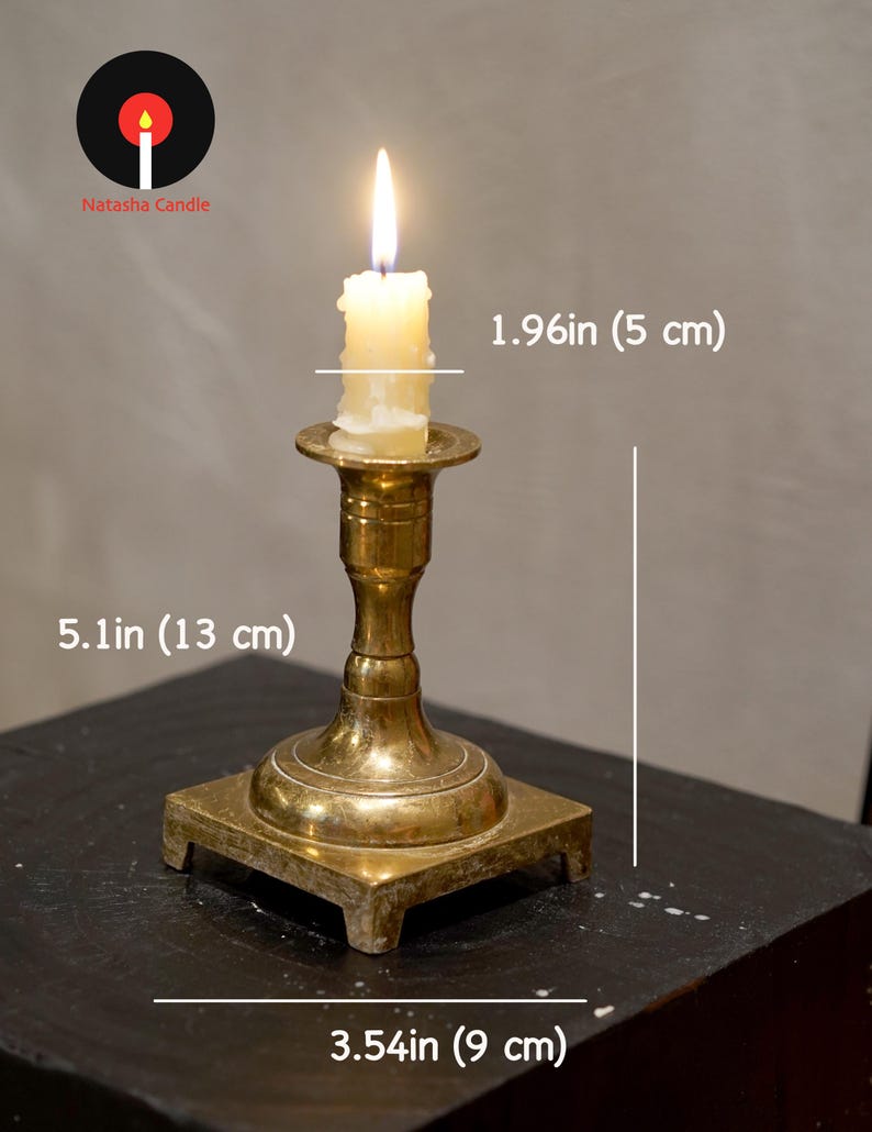 May include: A brass candlestick holder with a lit white candle. The holder has a square base measuring 3.54 inches wide and a total height of 5.1 inches. The candle has a diameter of 1.96 inches. The Natasha Candle logo is visible in the corner.