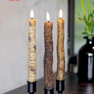 May include: Three decorative candles with realistic bark textures, each in a black metal candlestick. The candles have a warm, flickering glow. The Natasha Candle logo is in the upper left corner.
