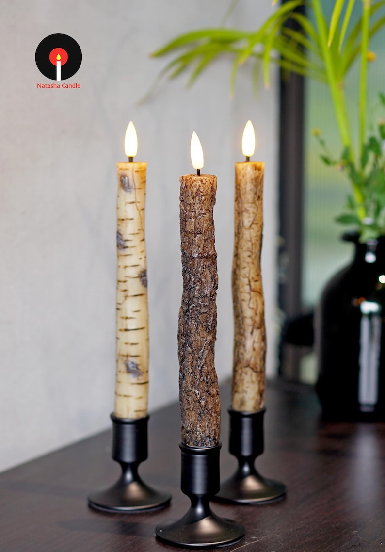 May include: Three decorative candles with realistic bark textures, each in a black metal candlestick. The candles have a warm, flickering glow. The Natasha Candle logo is in the upper left corner.