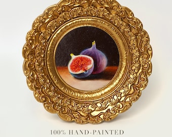 May include: A hand-painted, round framed artwork featuring two figs. One fig is whole, the other is cut open, revealing the red interior. The frame is gold with ornate detailing. The text at the bottom reads "100% HAND-PAINTED" and "FIGS".