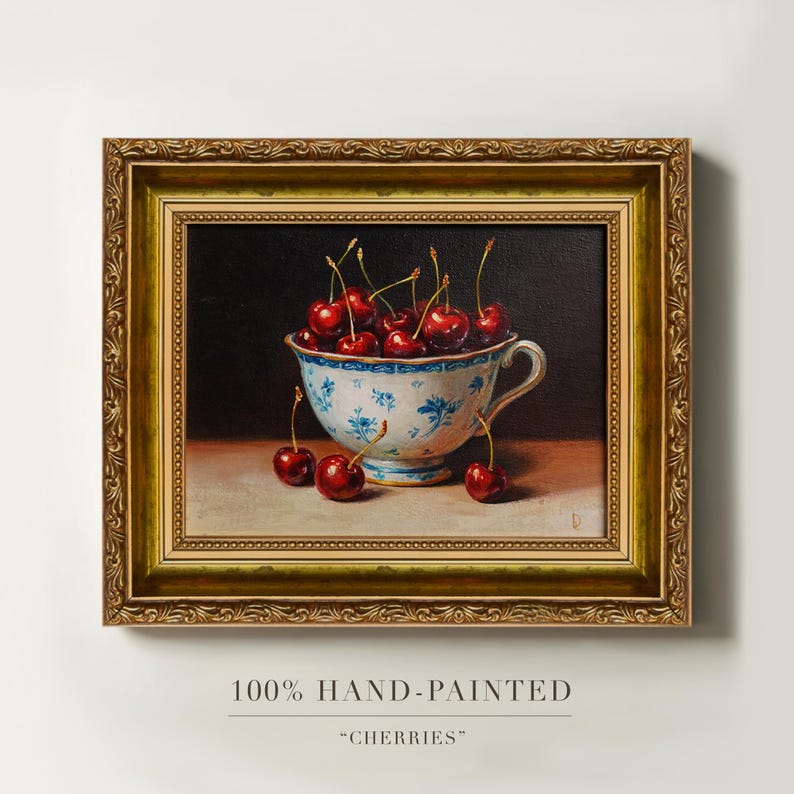 Puede incluir: Pintura enmarcada de una taza de t&eacute; llena de cerezas. La taza de t&eacute; tiene un dise&ntilde;o floral azul. Las cerezas son de color rojo intenso. El marco dorado es ornamentado. El texto en la parte inferior dice "100% HAND-PAINTED" y "CHERRIES".