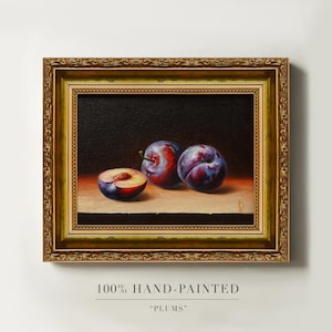 May include: An oil painting titled PLUMS featuring two whole dark purple plums and one halved plum with a visible pit, set against a dark background in a decorative ornate gold frame. The text 100% HAND-PAINTED PLUMS appears below the frame.