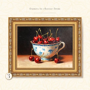 Puede incluir: Pintura enmarcada de cerezas en una taza de t&eacute; azul y blanca. Las cerezas son de color rojo intenso y la taza de t&eacute; tiene un dise&ntilde;o floral. El marco es dorado con detalles ornamentados. El texto en la parte superior dice "frames to choose from".