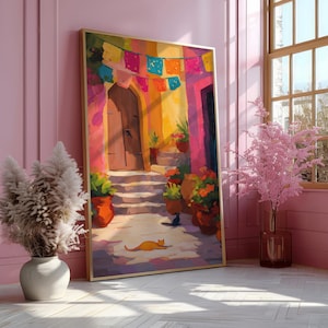 May include: A framed art print depicting a colorful courtyard scene. The artwork features a wooden door, steps, and potted plants, with a cat resting on the ground. A string of festive flags hangs overhead, and the scene is bathed in warm sunlight.