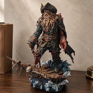 May include: A detailed figurine of a pirate captain with a tentacle beard, wearing a weathered tricorn hat and a dark coat. The figure stands on a wooden ship deck base surrounded by sculpted blue waves, featuring a large red crab claw hand.