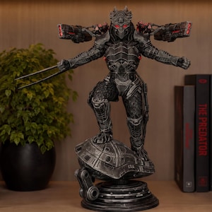 May include: A detailed dark gray Predator figurine standing on a metallic base. The character wears armored plating, features glowing red eyes, and has two shoulder-mounted cannons. One arm extends forward with sharp blades, while the other is open.