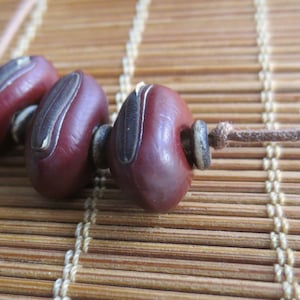 May include: A close-up of a necklace made with brown and black seed pods strung on a brown cord.
