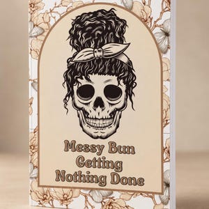 May include: A rectangular notebook with a white cover featuring a brown floral and butterfly pattern. The center displays an arched frame containing a black and white illustration of a skull with a messy bun and a bow, with the text Messy Bun Getting Nothing Done.