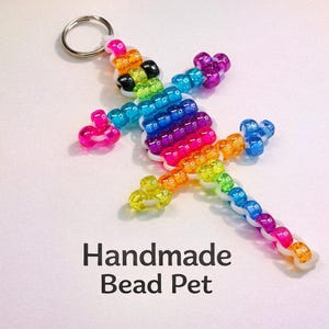 May include: A lizard-shaped keyring crafted from multicoloured plastic pony beads in a rainbow pattern, featuring a silver metal split ring at the top. The text Handmade Bead Pet is printed in black below the lizard figure on a white background.