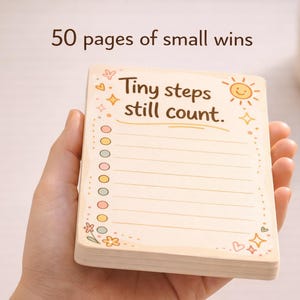 K&ouml;nnte beinhalten: Ein rechteckiger Notizblock mit 50 Seiten f&uuml;r kleine Erfolge, mit dem Text Tiny steps still count. Das cremefarbene Papier hat eine linierte Checkliste mit bunten runden Aufz&auml;hlungspunkten, einer l&auml;chelnden Sonne sowie kleinen Sternen und Herzen.