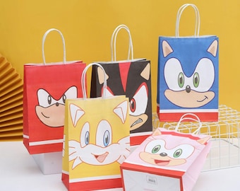 May include: A collection of colorful paper gift bags featuring cartoon character faces. The bags are red, yellow, blue, pink, and black, with white handles and red and white accents. The bags have different character faces.