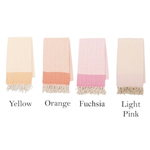 May include: A collection of six folded cotton towels in various colors. Each towel has a textured pattern and a contrasting solid-colored border with fringe. Colors include burgundy, yellow, orange, fuchsia, light pink, and lilac.