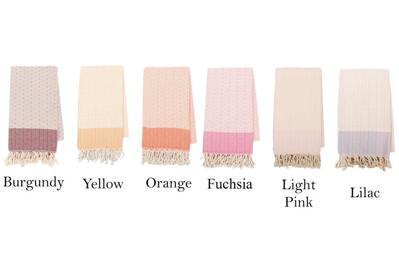 May include: A collection of six folded cotton towels in various colors. Each towel has a textured pattern and a contrasting solid-colored border with fringe. Colors include burgundy, yellow, orange, fuchsia, light pink, and lilac.