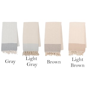 May include: A collection of six folded throws in various colors: black, gray, light gray, brown, light brown, and beige. Each throw has a textured pattern, a contrasting bottom border, and fringed edges. The color names are displayed below each throw.