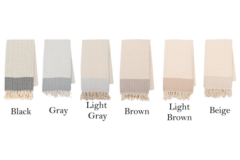 May include: A collection of six folded throws in various colors: black, gray, light gray, brown, light brown, and beige. Each throw has a textured pattern, a contrasting bottom border, and fringed edges. The color names are displayed below each throw.
