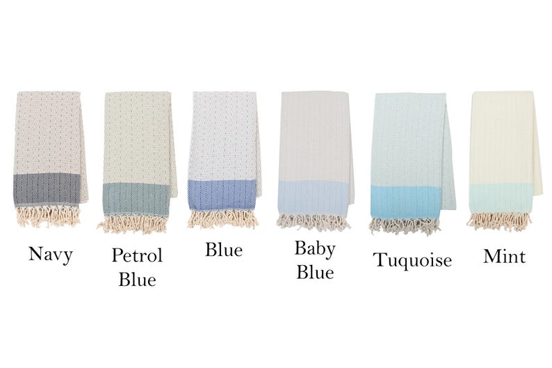 May include: Six folded cotton towels in various colors: navy, petrol blue, blue, baby blue, turquoise, and mint. Each towel has a contrasting color border and fringe.