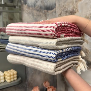 May include: A stack of four striped towels in red, white, and blue. The towels are folded and have tassels.
