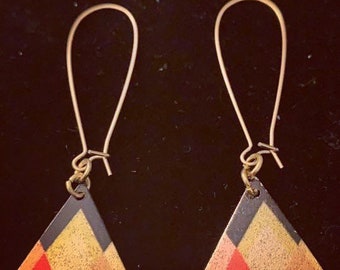 May include: A pair of gold triangle earrings with black and red geometric designs. The earrings have a simple, minimalist style.