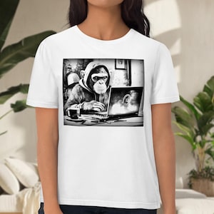 May include: A black and white image of a chimpanzee wearing a hoodie and using a laptop. The chimpanzee is sitting at a desk with a cup of coffee in front of it.