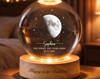 May include: A clear glass sphere lamp featuring an etched moon and star design, with the text "Sophia THE NIGHT YOU WERE BORN 22.11.1966". The sphere rests on a round wooden base engraved with the text "Happy 60th Birthday!" and emits a warm light.