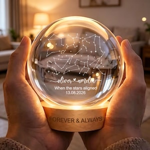 Könnte beinhalten: Ein kugelförmiges Glas-Nachtlicht auf einem runden Holzsockel. Das Glas zeigt eine weiße Sternbildkarte, die Namen oliver und amelia sowie den Text When the stars aligned 13.08.2026. Der Holzsockel ist mit FOREVER & ALWAYS graviert.