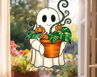 May include: A Halloween-themed hanging decoration featuring a smiling ghost holding a potted plant with three jack-o'-lanterns. The ghost is white with black eyes and a curved mouth. The plant has green leaves and orange pumpkins. The decoration hangs from a silver chain.
