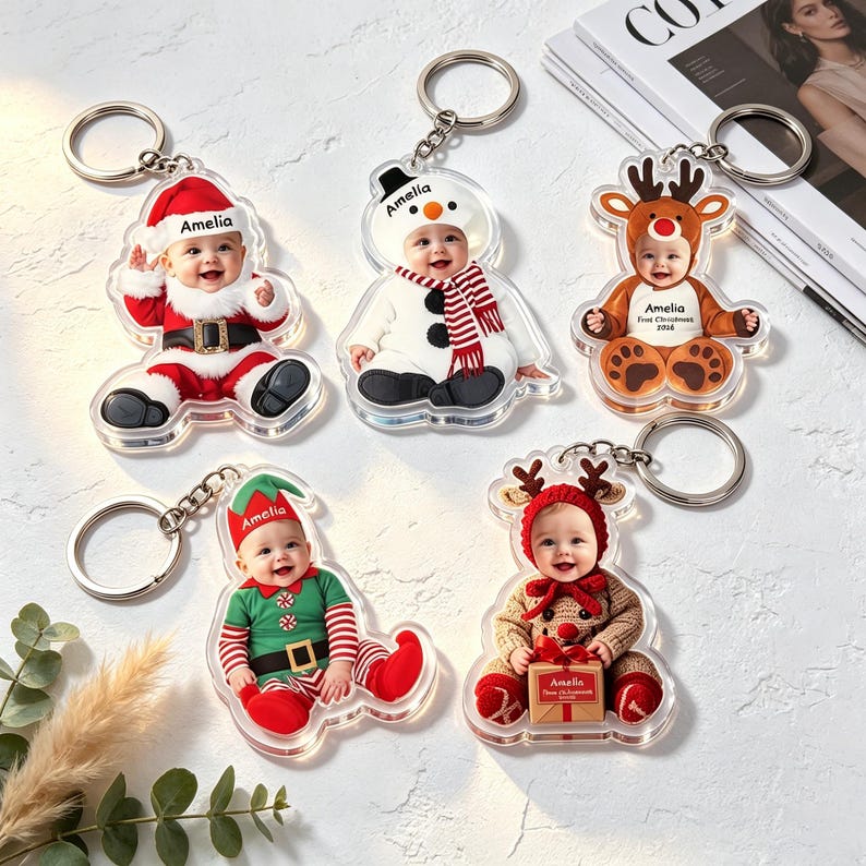 May include: Five clear acrylic keychains featuring photos of a baby named Amelia in various holiday costumes, including a Santa suit, a snowman outfit, a reindeer suit, an elf costume, and a winter outfit with a red hat and a gift box.