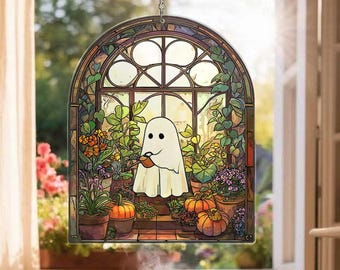 May include: A stained glass window decoration featuring a cartoon ghost smoking a pipe. The ghost is set against a backdrop of a window with plants and pumpkins. The window is framed with a decorative border and a silver chain for hanging.