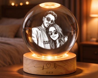 May include: A clear glass sphere lamp featuring an etched portrait of two people wearing sunglasses. The sphere rests on a round wooden base engraved with the letters j and b separated by a heart symbol and the date 5.12.18 below.