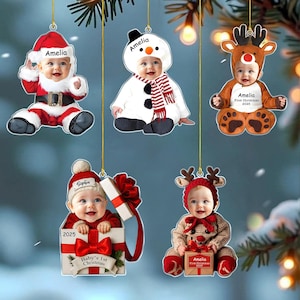 May include: Five personalized Christmas ornaments featuring photos of babies in holiday costumes. One shows a baby as Santa, one as a snowman, one as a reindeer, one in a gift box, and one in a reindeer hat holding a gift box with the name Amelia or Sophia.
