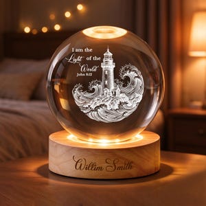 May include: A clear glass sphere lamp featuring an etched lighthouse and ocean wave design with the text I am the Light of the World John 8:12. The sphere rests on a circular light-up wooden base engraved with the name Willim Smith.