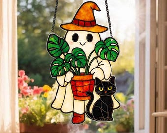 May include: Stained glass Halloween decoration featuring a friendly ghost wearing a witch hat, holding a potted plant, and accompanied by a black cat. The ghost is in a white sheet, and the cat has yellow eyes. The decoration hangs from a black chain.